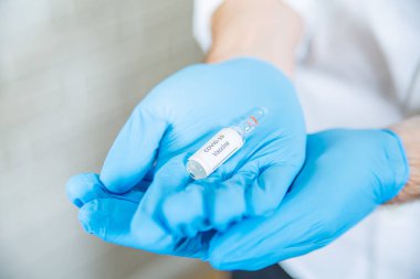 One COVID-19 vaccine bottle, vial, on a palm of hand in protective vinyl glove. A vaccination point. Fighting pandemic medical concept, composition.