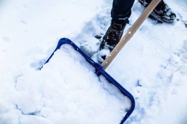 Kaldırımdan kar kürüyen bir manzara, açık mavi kar kürekli bir garaj yolu, soğuk güneşli bir günde..