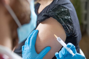 Erkek hemşire, sağlık çalışanı koruyucu eldivenler içinde, şırıngayla, iğne yaparken, kadın bir hastayı kolundan aşılarken. Aşı noktası. Savaş salgını konsepti.