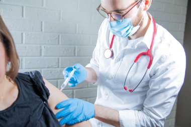 Bir erkek hemşire, koruyucu maskeli ve eldivenli bir doktor, iğne yapıyor, bir hastayı kolundan aşılıyor. Aşı noktası. Savaş salgını konsepti.