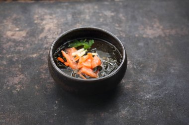 Somon, mevsimlik sebze ve Japon baharatlı bir balık çorbası. Siyah taşlı arka planda bir balık çorbası..