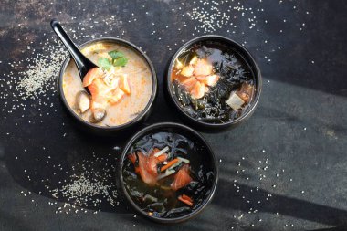 Siyah taşlı arka planda üç doğu çorbasından oluşan bir kompozisyon, üst görünüm.