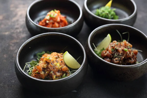 Tártaro de salmón, tártaro de atún, sobre un fondo pedregoso negro. Una composición de aperitivos. — Foto de Stock