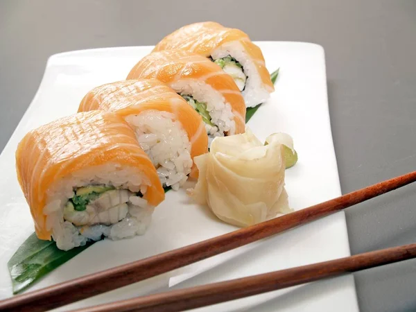 Sushi. California, rainbow rolls with salmon, pickled ginger, chopsticks on a white plate.