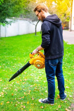 Bahçede kablosuz, elektrikli yaprak üfleyicisi kullanan sakallı genç bir adam. Bahçe işi. Sonbahar, sonbahar bahçıvanlığı arka bahçede, çimlerde, çimlerde çalışır..