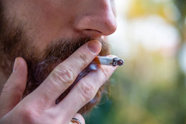 Close-up of a hand of a young adult man, holding a cigarette. Smoking break outdoor during a working day. Nicotine addiction.