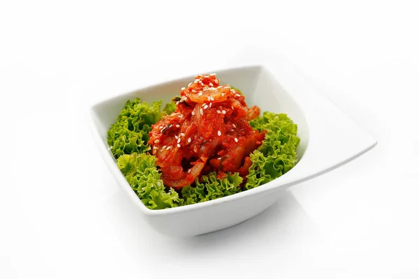Una ensalada de kimchi coreano sobre una lechuga decorativa verde, aislada sobre un fondo blanco. Un aperitivo oriental en un tazón, una foto para un menú de restaurante. — Foto de Stock
