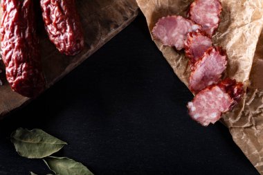 Kırsal bir kompozisyonun üst görüntüsü. Yiyecek ambalajında füme sosis, eski tarz ahşap bir tahta kesme tahtası, siyah taşlı tezgah. Polonyalı, ev yapımı bir sosis ve dilimler halinde kesilmiş..