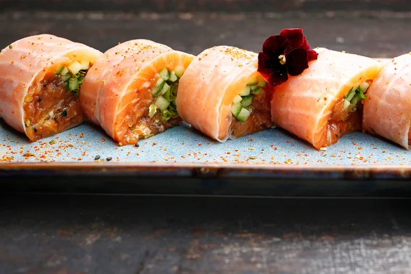 Sushi in forma rotolo. Maki di 6 pezzi in carta di riso con tartare di salmone, cetriolo, salmone, guarnito con fiore commestibile, su vassoio orientale, piatto, su fondo nero pietroso. Cucina giapponese delicatezza. — Foto Stock