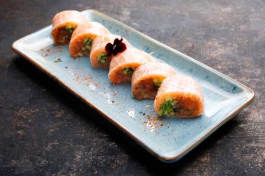 6 parça maki seti, somon, salatalık, pirinç kağıdı, yenilebilir çiçeklerle süslenmiş, doğu tepsisinde, tabakta, siyah taşlı arka planda. Suşi sığar. Japon mutfağı lezzeti..