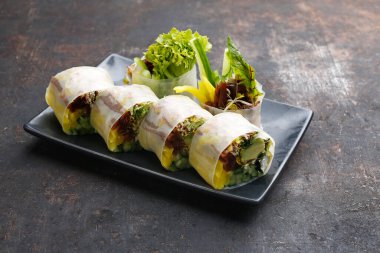 6 parça, vejetaryen sandviç, pirinç kağıdında suşi maki taze sebzeler ve Philadelphia peyniri, doğu tepsisinde, tabakta, siyah taşlı arka planda. Japon mutfağı lezzeti..