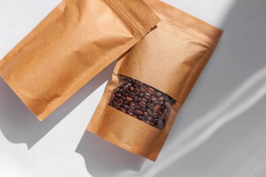 Kahverengi kese kağıtları kahve çekirdekli çantalar beyaz arka planda gölgelenmiş gölgeler. Yiyecek ve ürün şablonları için ambalaj mockup.Tokalı ve çay için pencereli paketler ağırlık bırakır