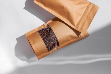 Kahverengi kese kağıtları kahve çekirdekli çantalar beyaz arka planda gölgelenmiş gölgeler. Yiyecek ve ürün şablonları için ambalaj mockup.Tokalı ve çay için pencereli paketler ağırlık bırakır