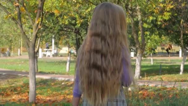 遊び場の屋外で長いブロンドの髪のジャンプを持つ美しい女の子 晴れた日には秋の公園で笑顔の子供が遊ぶ ワンピースだけで夢を歩いてかわいい幸せな子供 黄色の葉を持つ緑の草 — ストック動画