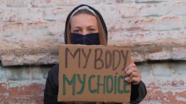 Genç kadın protestocu kartonda benim vücudumu tutuyor. Benim seçtiğim işaret orta parmağı gösteriyor. Kürtaj karşıtı yasaları protesto eden bir kız. Feminist kadınların güç yürüyüşü. Feminizm kavramı fırsat haklarına eşittir..