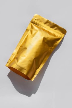 Üzerinde yiyecek ya da kahve çekirdekleri olan altın metalleştirilmiş çanta beyaz arka planda izole edilmiş sert gölgeli. Paketleme şablonu modeli. Çay yaprakları için tokalı paketler, ağırlık ürünleri düz yatıyordu.