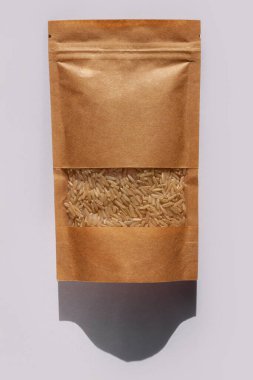 Kraft paper pouch bag with whole grain brown rice top view with harsh shadow on white background. Healthy diet food packaging mockup flat lay. Dry uncooked thai cereal high fiber magnesium antioxidant clipart