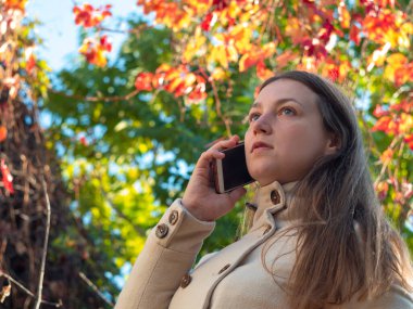 Güzel genç bayan cep telefonuyla konuşuyor. Deve kürklü ciddi bir kız renkli sonbahar doğası geçmişi var. Konsantre uzun saçlı iş kadını akıllı telefondan çağrıya cevap veriyor. Yaşam tarzı iletişimi