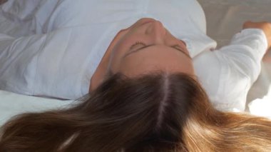 Sakin genç bir kadın rahat bir yatakta rahat bir şekilde uyur beyaz yumuşak yastıklarda ve sabah uyanır. Huzurlu sakin kız uykuya dalıyor. Sağlıklı uykuların tadını çıkarıyor. Uykusuzluk iyi geliyor.