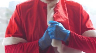 Santa Claus hold offers a gift box with ribbon bow in hands in protective gloves. Christmas shopping, New Year sales. Vibrant festive red color 4K video. Black Friday COVID-19 safe delivery concept.