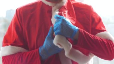 Santa Claus hold offers a gift box with ribbon bow in hands in protective gloves. Christmas shopping, New Year sales. Vibrant festive red color 4K video. Black Friday COVID-19 safe delivery concept.