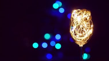 Noel masasında altın parıldayan çelenkle süslenmiş kristal şampanya bardağı arka planda Bokeh ışıkları. Birbirine aşık beyaz şarap çiftiyle romantik bir yeni yıl yemeği. Sihirli kış tatili atmosferi