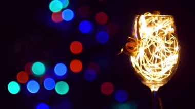 Noel masasında altın parıldayan çelenkle süslenmiş kristal şampanya bardağı arka planda Bokeh ışıkları. Birbirine aşık beyaz şarap çiftiyle romantik bir yeni yıl yemeği. Sihirli kış tatili atmosferi