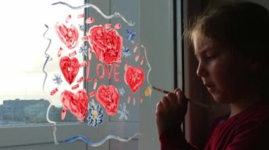 Küçük kız fırçayı elinde tutuyor ve cam camına kırmızı kalp çiziyor. Sevgililer günü, aşk, flört, karantina aile eğlencesi. Ev sanatları konsepti. Evde oynayan çocuk resimleri. Yeni normal.