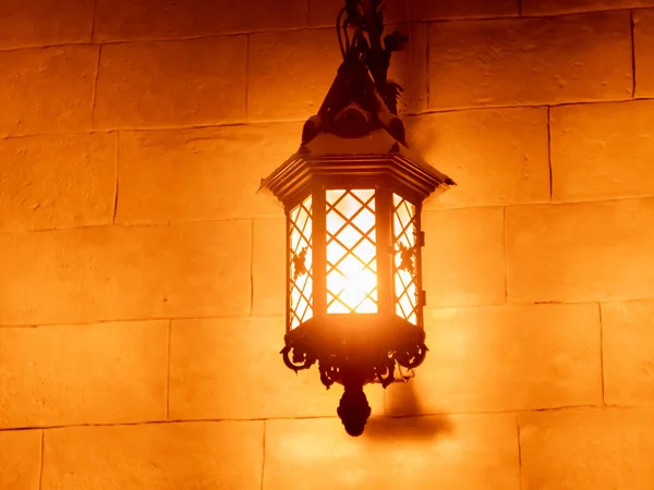 Outdoor old vintage lamp light glowing in the dark. Beautiful dusty lantern hang in front of house in the night. Exterior lighting, external illumination on textured wall. Retro style wallpaper.