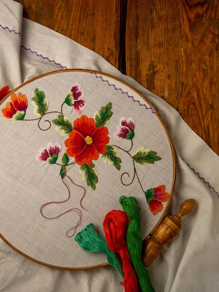 Flowers embroidery on white textile in hoop wooden background. Traditional ukrainian floss stitch embroidery motifs. Handmade ethnic clothes towel tablecloth. New normal lockdown hooby crafts tutorial