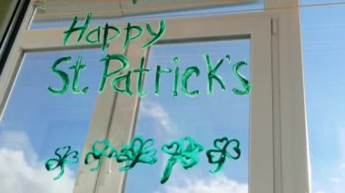 St. Patrick 's Day Man' in üç yapraklı yeşil yoncaları, şenlikli ev dekorasyonu, karantina aile eğlencesi çizimi. Babam pencere camına yonca yaprakları çizer. Ev konseptini koru Yeni normal