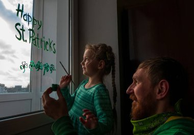 Üç yapraklı yeşil yoncalar, şenlikli ev dekorasyonu ve aile eğlencesi çizen kızıyla Aziz Patrick Günü Baba 'yı çizmek. Pencere camına yonca yaprağı çizmek. Ev konseptini koru Yeni normal