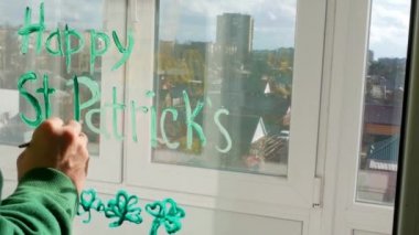 St. Patrick 's Day Man' in üç yapraklı yeşil yoncaları, şenlikli ev dekorasyonu, karantina aile eğlencesi çizimi. Babam pencere camına yonca yaprakları çizer. Ev konseptini koru Yeni normal