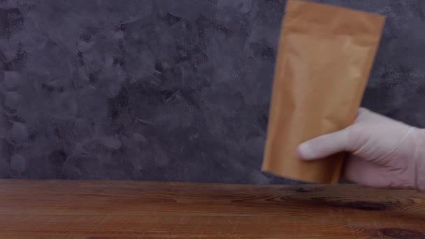 手拿着防护手套拿着褐色牛皮纸袋和咖啡豆木制背景的4K模型 食品交付包装模板 包装与卡环窗茶叶重量产品 — 图库视频影像