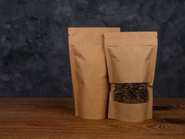 Çanta maketi. Kahveli, kahverengi kraft kağıtlı kahve çekirdeği ahşap arka planda fotokopi alanı. Toka şablonlu ambalaj yiyecek teslimatı çay ağırlıklı ürün bırakır. Mağaza satış reklam tasarımı.