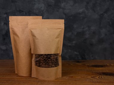 Çanta maketi. Kahveli, kahverengi kraft kağıtlı kahve çekirdeği ahşap arka planda fotokopi alanı. Toka şablonlu ambalaj yiyecek teslimatı çay ağırlıklı ürün bırakır. Mağaza satış reklam tasarımı.