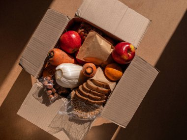 Sağlıklı yemek teslimatı katı gölgeler altında kaldı. Doğal organik ürünler paketini çıkarın. Bağış kutusu Yeni normal online alışveriş güvenli teslimat konsepti. Meyve sebzeleri, havuç, elma, ekmek, fındık.