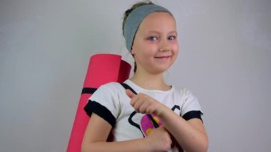 Küçük gülümseyen kız pembe yoga minderi gri arka plan. Çocukların esnekliği için yoga. Zihinsel sağlık, aktif yaşam tarzı, spor fitness sınıfı. Evde esneme eğitimi var. Yeni normal