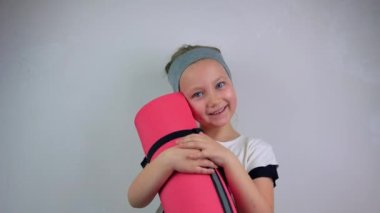 Küçük gülümseyen kız pembe yoga minderi gri arka plan. Çocukların esnekliği için yoga. Zihinsel sağlık, aktif yaşam tarzı, spor fitness sınıfı. Evde esneme eğitimi var. Yeni normal