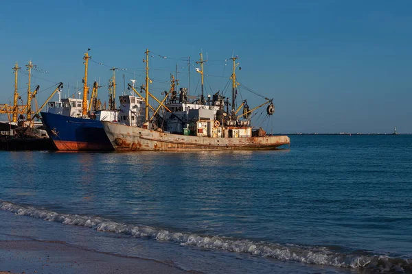 Old ships at the pier on the sea with an empty beach with clear blue water and sky. Seaport on the shore with cranes and boats. Wallpaper for desktop, poster, marine travel photo for post card design.