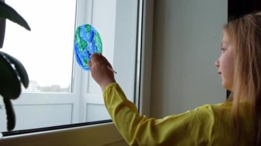 Ev 4K 'nin penceresine gezegeni boyayan sevimli küçük kız. 22 Nisan Dünya Günü 'nüz kutlu olsun. Yaratıcı aile eğlencesi yeni gerçekliği kilitliyor. Çevrenin bilinçli tüketim kavramının korunması