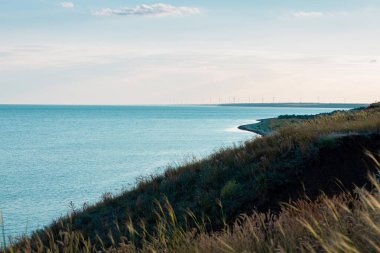 Boş bir sahilde inanılmaz renkli bir gökyüzü. Arka planda rüzgar türbinleri olan deniz kıyısı. Masaüstü için yaz duvar kağıdı, poster, kartpostal tasarımı için deniz yolculuğu fotoğrafı. Yeşil enerji eko kavramı.