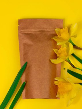 Kahverengi kese kağıdı, kahve çekirdekleri ve pastel arka planda sarı nergis çiçekleri. Gıda ürün şablonu için paketleme. Çay yaprakları için kopçayla paketleme, düz ağırlık kopyalama alanı