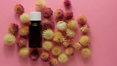 Bitki özlü cam şişenin arka planında pembe çiçekler var. Alternatif tıp cilt bakım spa aroma terapisi, vücut tedavisi, boş güzellik kozmetik ürün şablonu. Masaj yağı, cilt bakımı