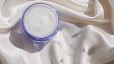 Pürüzsüz ipek arka plan üzerine mavi cam krem kavanozu çiçek gölgesi 4K Doğal cilt nemlendirici kozmetik, sağlıklı cilt SPA sağlıklı yüz hidrasyon tedavisi UV