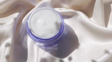 Pürüzsüz ipek arka plan üzerine mavi cam krem kavanozu çiçek gölgesi 4K Doğal cilt nemlendirici kozmetik, sağlıklı cilt SPA sağlıklı yüz hidrasyon tedavisi UV