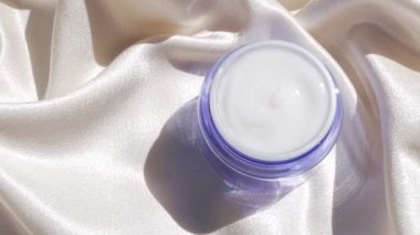 Pürüzsüz ipek arka plan üzerine mavi cam krem kavanozu çiçek gölgesi 4K Doğal cilt nemlendirici kozmetik, sağlıklı cilt SPA sağlıklı yüz hidrasyon tedavisi UV