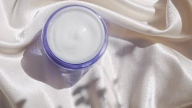 Pürüzsüz ipek arka plan üzerine mavi cam krem kavanozu çiçek gölgesi 4K Doğal cilt nemlendirici kozmetik, sağlıklı cilt SPA sağlıklı yüz hidrasyon tedavisi UV