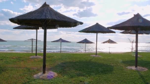 緑の芝生 砂のビーチ 鮮やかな青い海の水と太陽の光で空の背景にわら傘 風景4K映像 夏休みの季節の熱帯海洋旅行の残りの部分 リゾート広告 — ストック動画