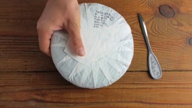 Shu Puerh keki Çin mayalanmış siyah çayı beyaz kağıtta bıçakla. Erkek ellerinin elinde çip kırıkları eski yuvarlak, olgunlaşmış siyah pu-erh parçaları. Sağlıklı canlandırıcı içecekler..